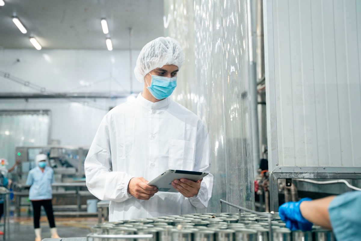 Empleado de la industria alimentaria protegido con gorro, bata, cubrebarbas y cubrezapatos